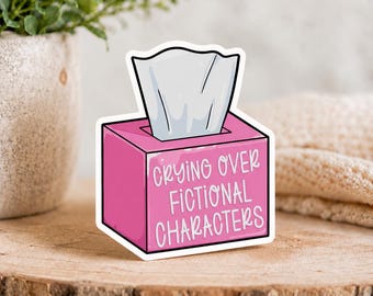 Puede incluir: Una pegatina rectangular de color rosa con forma de caja de pañuelos y un pañuelo blanco saliendo por la parte superior. El frente de la caja tiene el texto blanco "CRYING OVER FICTIONAL CHARACTERS" en letra manuscrita con borde blanco.