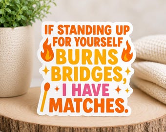 Pode incluir: Um autocolante branco com o texto "IF STANDING UP FOR YOURSELF BURNS BRIDGES, I HAVE MATCHES." O texto é em laranja, amarelo e rosa, com gráficos de chamas e fósforos. O autocolante está numa superfície de madeira.