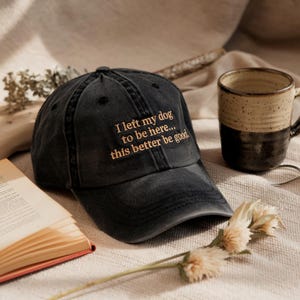 May include: A black baseball cap with a gold embroidered message that reads "I left my dog to be here... this better be good."