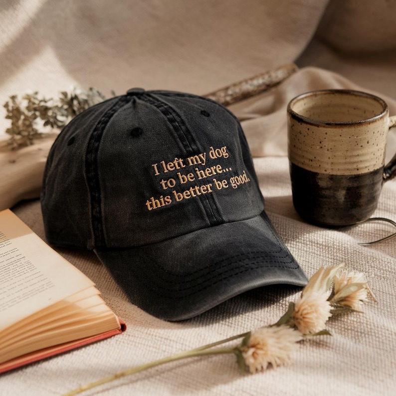 May include: A black baseball cap with a gold embroidered message that reads "I left my dog to be here... this better be good."
