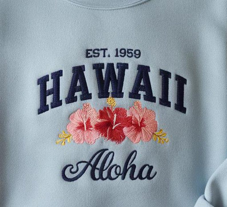 May include: Light blue sweatshirt with embroidered text "EST. 1959 HAWAII Aloha" and floral accents.