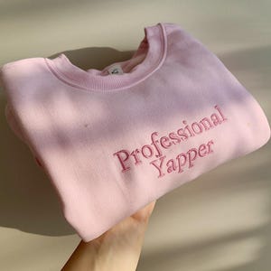 May include: A pink sweatshirt with the text "Professional Yapper" embroidered in pink.