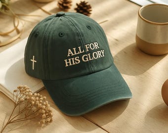 May include: A dark green baseball cap with the text "ALL FOR HIS GLORY" embroidered in white. A white cross is embroidered on the side. The cap has a curved brim and a button on top.