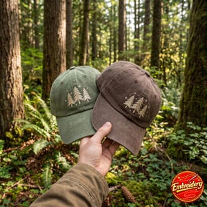 May include: Two baseball caps, one in olive green and one in brown, each featuring an embroidered design of three pine trees surrounded by small star accents. The caps have a structured crown, a curved brim, and stitched eyelets on the panels.