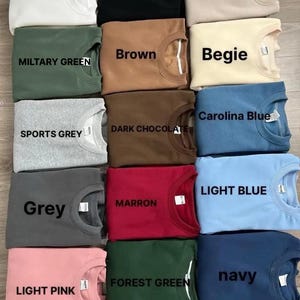 May include: A color chart of 12 different sweatshirt colors. The colors are: White, Black, Sand, Brown, Military Green, Begie, Sports Grey, Dark Chocolate, Carolina Blue, Grey, Marron, Forest Green, Light Pink, Light Blue, and Navy.