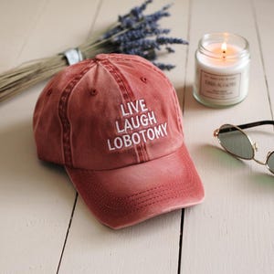 May include: A red baseball cap with the text "LIVE LAUGH LOBOTOMY" embroidered in white.