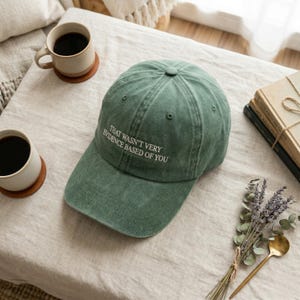 May include: A green baseball cap with the text "THAT WASN'T VERY EVIDENCE BASED OF YOU" in white. The cap is made of a soft material and has a curved brim. The hat is on a neutral-coloured surface.