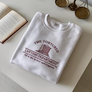May include: White sweatshirt with a maroon graphic print of a building with the text "The Tortured Lawyers Department" and "All is fair in love and litigation".