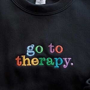 May include: Black sweatshirt with the phrase "go to therapy." embroidered in rainbow colors.