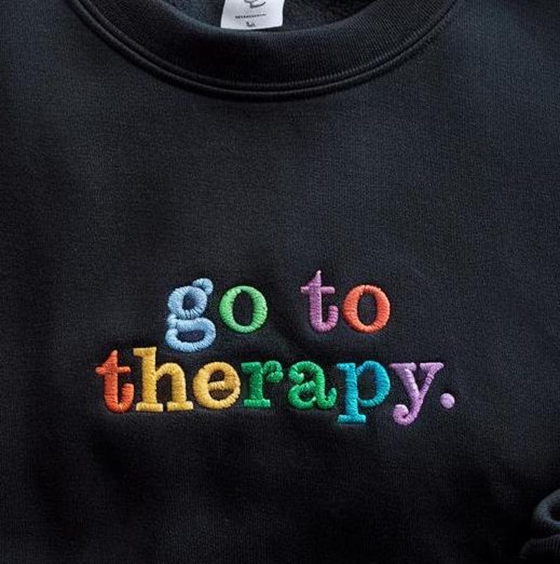 May include: Black sweatshirt with the phrase "go to therapy." embroidered in rainbow colors.