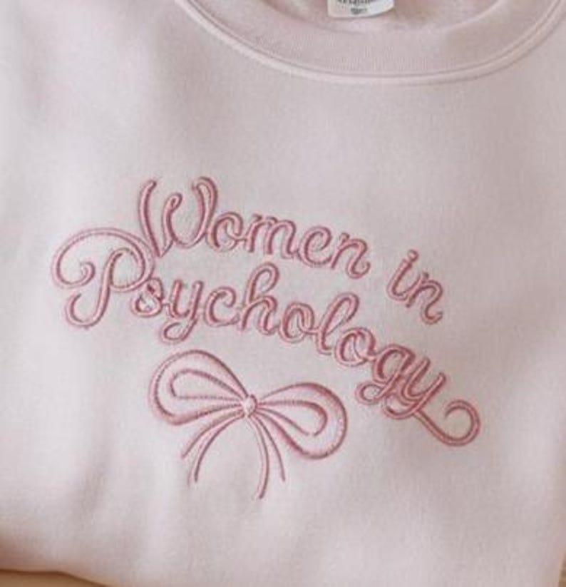 May include: A pink sweatshirt with the text "Women in Psychology" embroidered in pink script with a pink ribbon below the text.