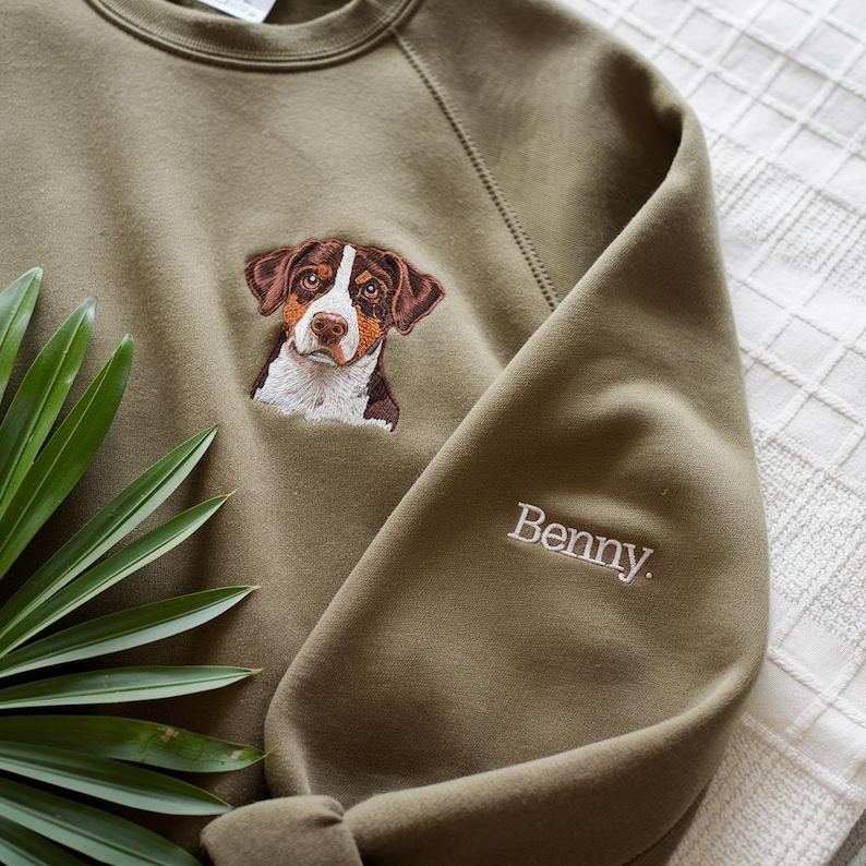 May include: A green sweatshirt with an embroidered image of a brown and white dog with the name "Benny" embroidered on the sleeve.