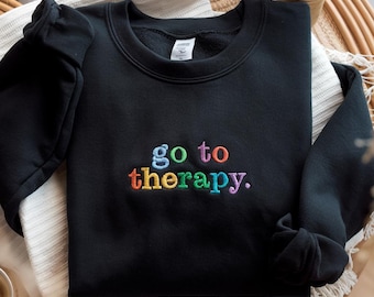May include: Black sweatshirt with the phrase "go to therapy" embroidered in rainbow colors.