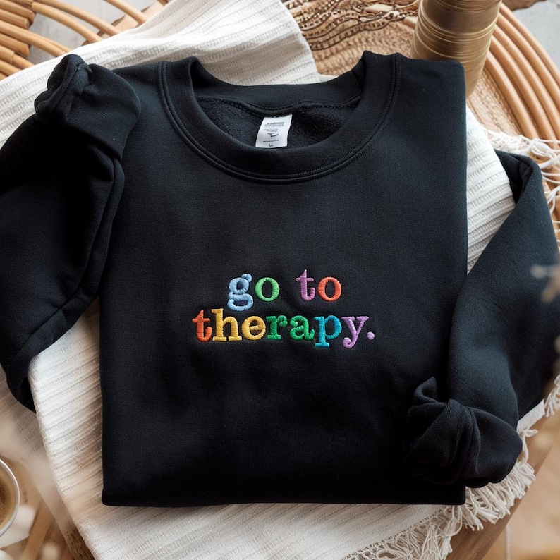 May include: Black sweatshirt with the phrase "go to therapy" embroidered in rainbow colors.