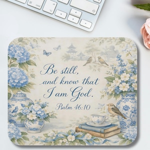 May include: A decorative mousepad with a floral and bird design, featuring the text "Be still, and know that I am God. Psalm 46:10." The design includes blue hydrangeas, butterflies, and a teacup.