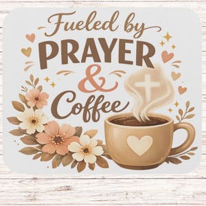 May include: A white mousepad with the text "Fueled by Prayer & Coffee" in brown and peach lettering. A coffee cup with a heart and steam with a cross design is featured. Floral and heart accents complete the design.