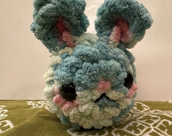 Op de afbeelding: Een blauwe en roze pluche konijn met zwarte ogen. Het konijn is gemaakt van garen en heeft een zachte, knuffelige textuur.