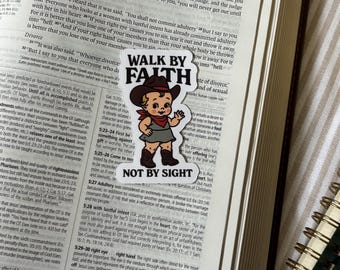 May include: A sticker on an open book with the text "WALK BY FAITH" and "NOT BY SIGHT". The sticker shows a cartoon baby in a cowboy hat and boots, with a red scarf.