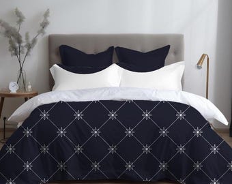May include: A navy blue and white patterned duvet cover and pillow set. The duvet cover features a geometric design with white snowflake-like shapes on a dark blue background. The set includes two navy blue and two white pillows.