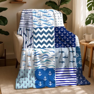 May include: A nautical-themed throw blanket with a patchwork design. The blanket features various blue and white patterns, including anchors, sailboats, waves, and stripes. The blanket is draped over a beige armchair.