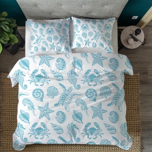 May include: White bedding set featuring a light blue pattern of marine life, such as starfish, crabs, seahorses, and turtles. The set includes a duvet cover and two pillowcases, creating a coastal theme.