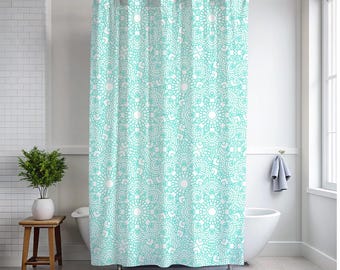 Puede incluir: Cortina de ducha estampada en turquesa y blanco con un diseño de mandala repetido. La cortina cuelga en un baño, con una bañera blanca y un pequeño taburete de madera con una planta.
