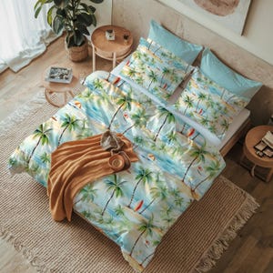 Pode incluir: Uma cama com edredão e fronhas com tema tropical com palmeiras, veleiros e uma cena de praia em tons de azul, verde e branco. Um cobertor castanho, um chapéu pequeno e uma chávena estão na cama.