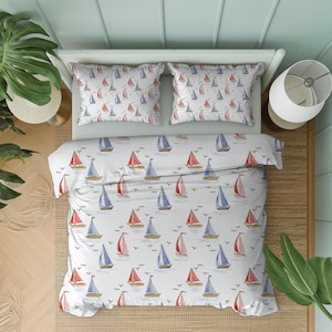 Op de afbeelding: Wit beddengoed met een nautisch thema, met een patroon van rode en blauwe zeilboten op een lichtblauwe zee. De set bevat een dekbedovertrek en twee kussenslopen, perfect voor een slaapkamer met een kustthema.