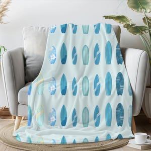 Op de afbeelding: Een zachte blauwe deken met een herhalend patroon van blauwe surfplanken op een lichtblauwe achtergrond.