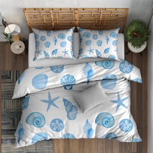 May include: White bedding set with a blue seashell pattern, including a duvet cover, two pillowcases, and a gray accent pillow. The design features starfish, conch shells, and sand dollars. The bed has a woven headboard.