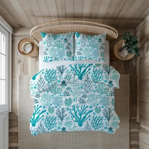 Könnte beinhalten: Ein Bett mit einer weißen Bettdecke und zwei passenden Kissenbezügen, alle mit einem türkisfarbenen und marineblauen Korallenriffmuster. Das Bett steht auf einem gewebten Teppich, mit einem hölzernen Kopfteil und Nachttischen. Der Raum hat ein Küstenmotiv.