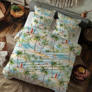 Op de afbeelding: Een tropische beddenset met een strandscène met palmbomen, surfplanken en parasols. Het dekbedovertrek en de kussenslopen hebben een lichtblauw en groen kleurenpalet, wat een ontspannen en zomerse sfeer creëert. De set bestaat uit een dekbedovertrek en kussenslopen.