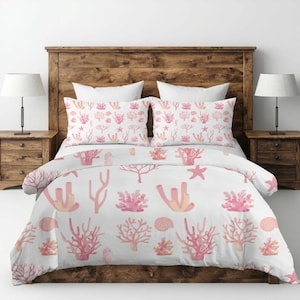 Könnte beinhalten: Weißes Bettwäsche-Set mit einem Korallenriffmuster in Rosa- und Pfirsichtönen. Das Set enthält einen Bettbezug und zwei Kissenbezüge mit verschiedenen Korallenformen, Seesternen und Muscheln. Das Bett steht vor einem hölzernen Kopfteil.