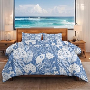 May include: A blue and white floral patterned bed set, including a duvet cover and two pillowcases. The design features large tropical leaves and flowers. The bedding is on a wooden bed frame, with a view of the ocean in the background.