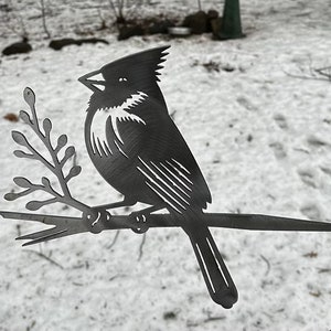 May include: Metal silhouette of a cardinal perched on a branch. The cardinal is black and has a white chest. The branch is also black and has small leaves.