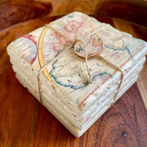 May include: Set of four square coasters featuring a vintage world map design. The coasters are made of a light beige stone material and are tied together with twine.