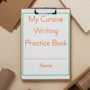 May include: A brown clipboard with a white sheet of paper that says "My Cursive Writing Practice Book" with a line for a name. The clipboard is on a beige surface with other craft supplies.