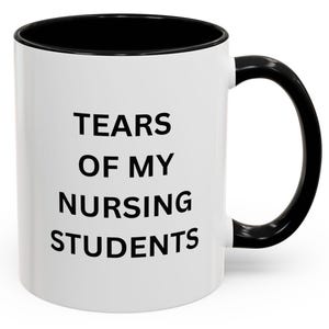 May include: White ceramic coffee mug with a black rim and handle. The mug has black text that reads "TEARS OF MY NURSING STUDENTS".