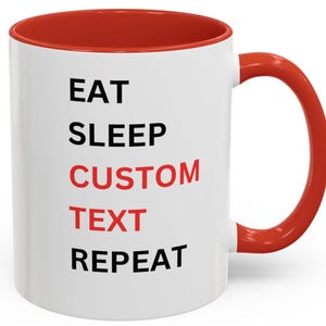 May include: White ceramic coffee mug with a red rim and handle. The mug has black text that reads "EAT SLEEP CUSTOM TEXT REPEAT" with the word "CUSTOM" in red.