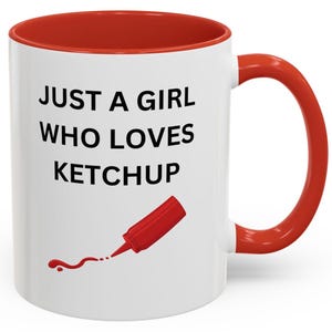 Puede incluir: Taza de cerámica blanca con interior y asa rojos. La taza presenta el texto "JUST A GIRL WHO LOVES KETCHUP" en negro, junto con una ilustración de una botella de ketchup roja.