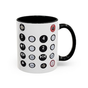 May include: White ceramic mug with a black interior and handle. The mug is decorated with a design of elevator buttons, including numbers, directional arrows, and other symbols. A novelty item.