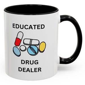 May include: White ceramic mug with a black rim and handle. The mug has black text that reads "EDUCATED DRUG DEALER" and a cartoon image of colourful pills.
