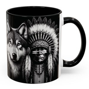 May include: Black and white ceramic mug featuring a detailed illustration of a wolf and a Native American chief wearing a feathered headdress. The mug has a black interior and handle, with a white exterior. The design is a striking contrast against the white background.