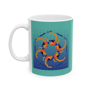 Puede incluir: Taza de cerámica blanca con fondo turquesa que presenta un gráfico de seis nadadoras sincronizadas formando un círculo en una piscina azul. Las nadadoras llevan trajes de baño naranja y azul.