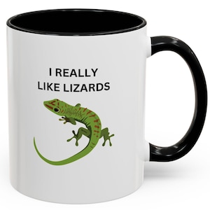 May include: White ceramic mug with a black rim and handle. The mug has a green lizard with red markings on it and the text "I REALLY LIKE LIZARDS" printed on it.
