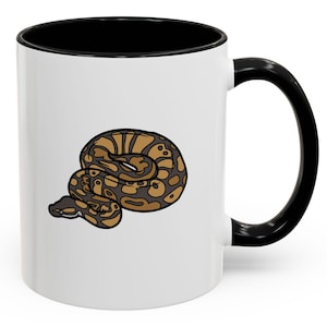 Könnte beinhalten: Weiße Keramik-Kaffeetasse mit schwarzem Rand und Henkel. Die Tasse zeigt eine Cartoon-Illustration einer braunen und schwarzen Schlange, die sich zusammengerollt hat.