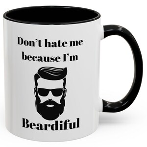 Puede incluir: Taza de café de cerámica blanca con borde y asa negros. La taza tiene una ilustración en blanco y negro de un hombre con barba y gafas de sol. El texto "Don't hate me because I'm Beardifull" está impreso en la taza.