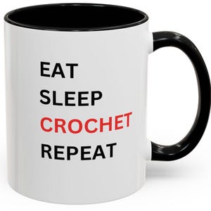 May include: White ceramic coffee mug with a black rim and handle. The mug has black text that reads "Eat Sleep Crochet Repeat" with the word "Crochet" in red.