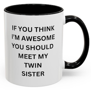 Op de afbeelding: Een witte keramische koffiemok met een zwarte rand en handvat. De mok heeft zwarte tekst met de tekst "Als je denkt dat ik geweldig ben, moet je mijn tweelingzus ontmoeten."