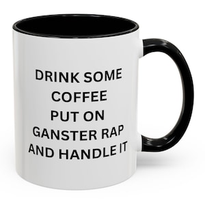 Pode incluir: Caneca de café branca com borda e alça pretas. A caneca tem texto preto que diz "Drink some coffee put on gangster rap and handle it."